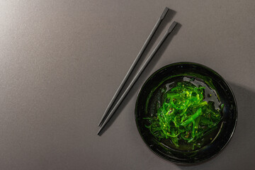 Wakame seaweed salad with sesame seeds and chili pepper in a bowl. Trendy hard light, dark shadow