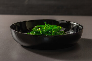 Wakame seaweed salad with sesame seeds and chili pepper in a bowl. Trendy hard light, dark shadow