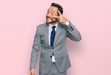 Middle age man wearing business clothes doing peace symbol with fingers over face, smiling cheerful showing victory