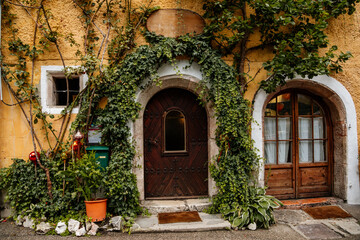 Fototapeta na wymiar Hallstatt, Austria, 27 August 2021: Colorful scenic picturesque town street at summer day, oval wooden door, braided window, green ivy at yellow wall, traditional historical house, village near lake