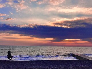 Obraz premium Stunning seascape. The rider on a horse at sunset on the beach. The person horse riding.