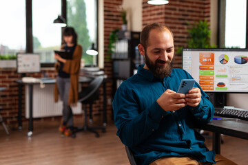 Businessman holding smartphone looking on social media texting with remote friends in startup company office. Manager searching business information developing online communication app.