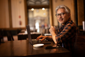 Businessman working on laptop in cafe. Handsome senior man enjoying in fresh coffee.