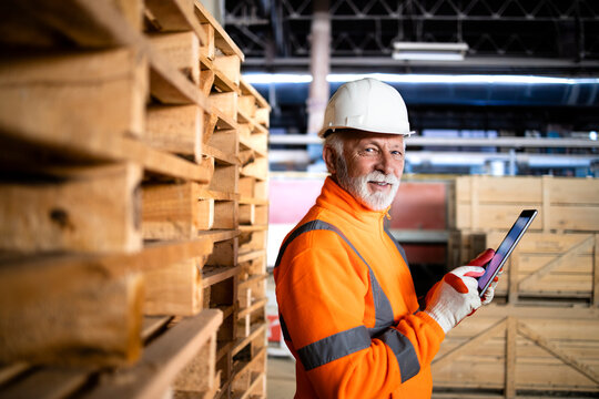 Warehouse worker in safety equipment and hard hat holding tablet computer and managing goods dispatching.