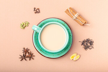 Obraz na płótnie Canvas Healthy Indian beverage masala chai - tea hot drink with milk and spices in rustic green teacup with ingredients for making masala chai from above on simple beige minimal background 