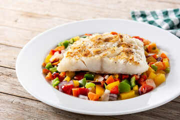 Grilled cod with vegetables in plate on wooden table	