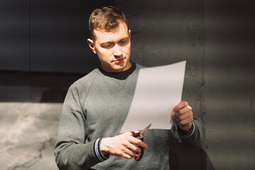 a man cuts a white sheet of paper with scissors from the bottom up