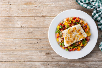 Grilled cod with vegetables in plate on wooden table. Top view. Copy space	