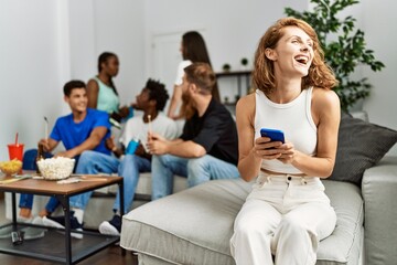 Group of young friends smiling happy sitting on the sofa. Woman using smartphone at home.