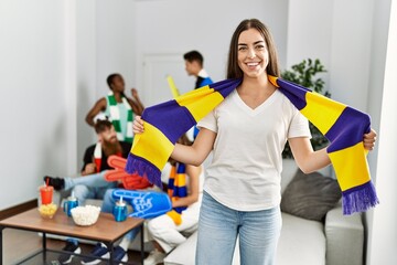 Young soccer hooligan woman smiling happy holding team scarf at home