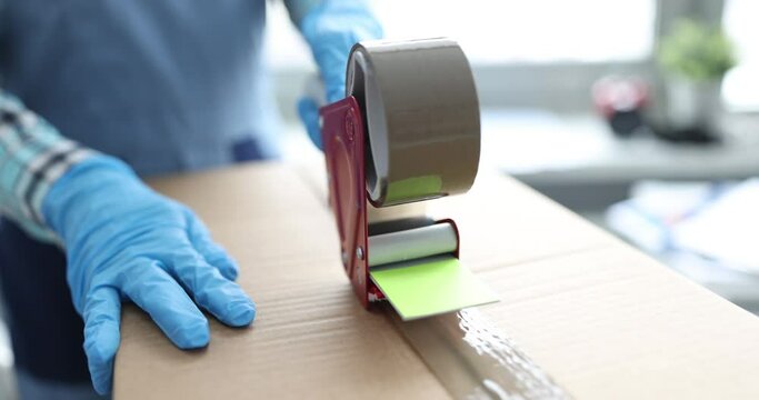 Postal worker packing cardboard boxes with tape closeup