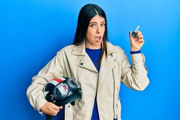 Young hispanic woman holding motorcycle helmet and key clueless and confused expression. doubt concept.