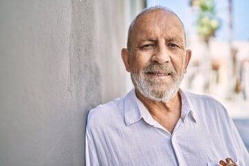 Senior man smiling confident leaning on wall at street