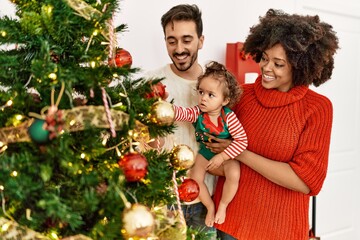 Couple and daughter smiling confident decorating christmas tree at home