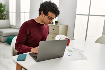 Young hispanic man using laptop working at home.