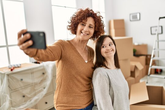Mature mother and down syndrome daughter moving to a new home, standing by cardboard boxes taking a selfie picture