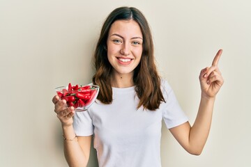 Young brunette woman holding red peppers smiling happy pointing with hand and finger to the side