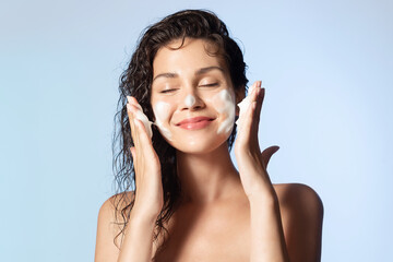Smiling young woman washing foam face by natural foamy gel. Satisfied girl with bare shoulders applying cleansing beauty product on cheeks closed eyes. Personal hygiene, skincare daily routine. - obrazy, fototapety, plakaty
