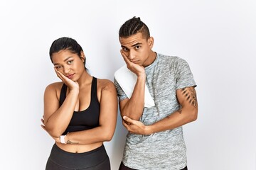 Young latin couple wearing sportswear standing over isolated background thinking looking tired and bored with depression problems with crossed arms.