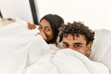 Obraz premium Young latin couple covering with bedsheet lying on the bed at bedroom.
