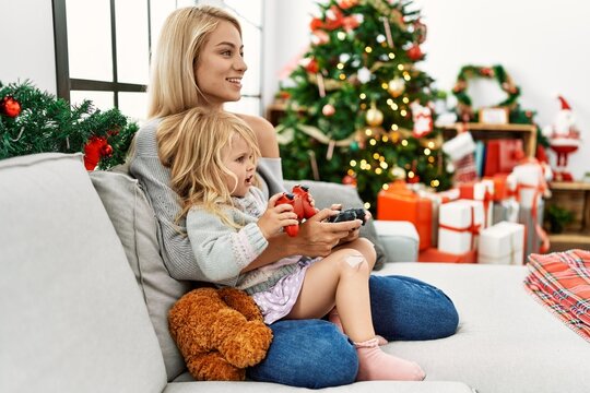 Mother and daughter playing video game sitting by christmas tree at home