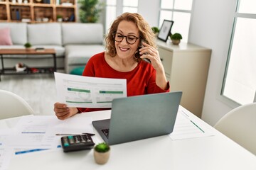 Middle age caucasian woman talking on the smartphone working at home.