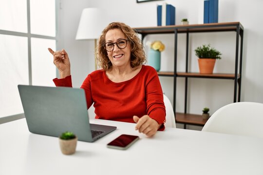 Middle age caucasian woman using laptop sitting on the table at home smiling happy pointing with hand and finger to the side