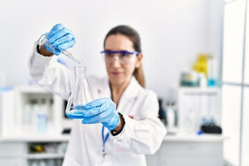 Fototapeta premium Young hispanic woman wearing scientist uniform holding test tube at laboratory