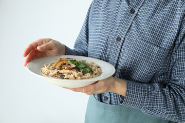 Woman in apron holds plate of risotto with mushrooms