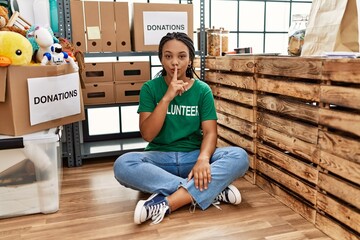 Young african american woman wearing volunteer t shirt at donations stand asking to be quiet with...