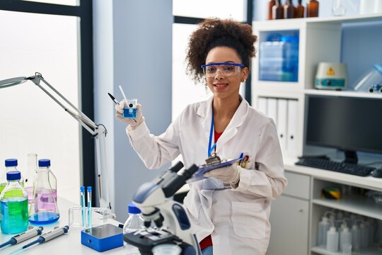 Young african american woman wearing scientist uniform holding test tube at laboratory