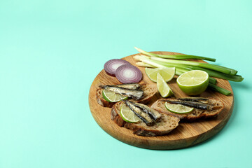 Board with sandwiches with sprats on mint background