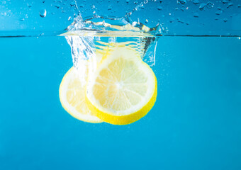 Cut fresh lemons in clear water with splash, blue background