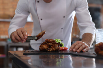Professional chef with delicious fried chicken wings in restaurant kitchen, closeup