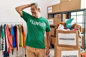 Middle age hispanic man wearing volunteer t shirt at donations stand smiling confident touching...