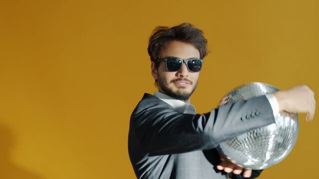 Slow motion portrait of good-looking Arab guy enjoying party dancing with mirrorball on yellow background. Celebration and disco ball concept.