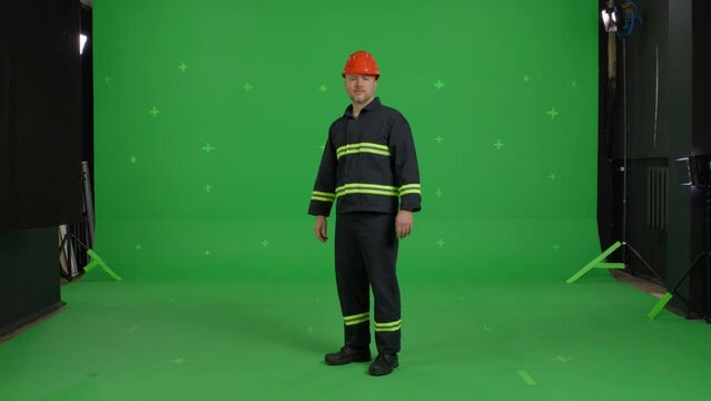 Handsome man in working robe and construction helmet look on the camera over green screen background. Chroma Key 4k video footage