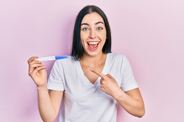 Beautiful woman with blue eyes holding pregnancy test result smiling happy pointing with hand and finger