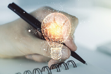 Double exposure of creative light bulb hologram with hand writing in diary on background, research...