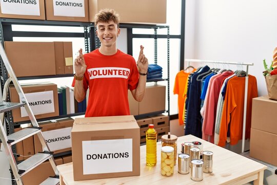 Young caucasian man volunteer holding donations box gesturing finger crossed smiling with hope and eyes closed. luck and superstitious concept.