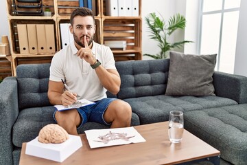 Handsome hispanic man working with rorschach test at psychology clinic asking to be quiet with...