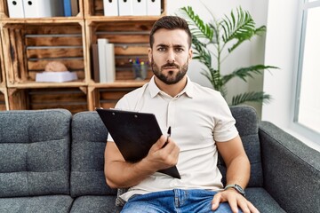 Handsome hispanic man holding clipboard working at psychology clinic skeptic and nervous, frowning upset because of problem. negative person.