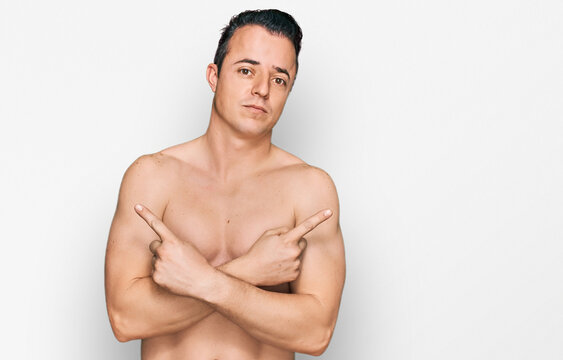 Handsome young man wearing swimwear shirtless pointing to both sides with fingers, different direction disagree