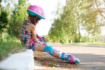 A girl in a helmet and roller skates puts on knee pads to protect against falls, injuries and...