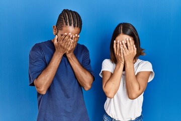 Young hispanic couple standing together with sad expression covering face with hands while crying....