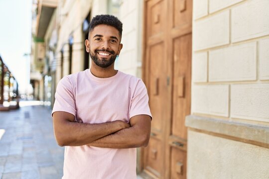 Handsome hispanic man smiling happy with crossed arms outdoors. Young friendly guy standing at the street with cheerful face.