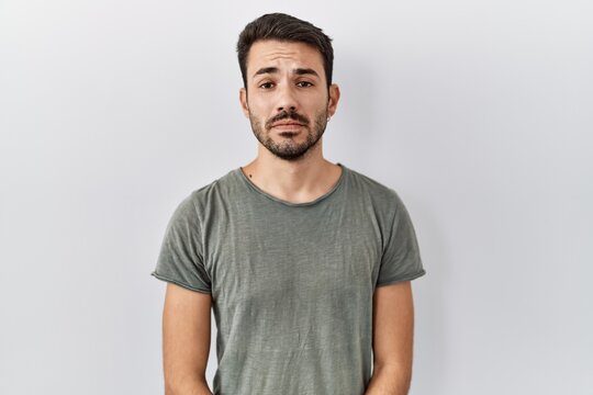 Young hispanic man with beard wearing casual t shirt over white background depressed and worry for distress, crying angry and afraid. sad expression.