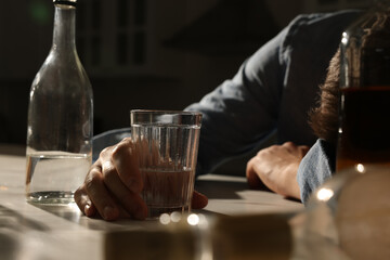 Addicted man with alcoholic drink sleeping at table in kitchen, closeup