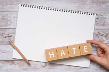 「HATE」と書かれた積み木とペン、ノート、人の手