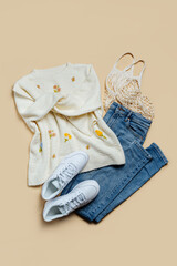 Cute  jumper with jeans and white sneakers on beige background. Stylish autumn or spring  clothes. Fashion concept. Flat lay, top view.